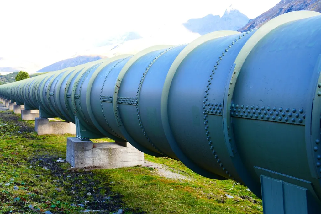 Large-diameter industrial pipeline running above ground, supported by concrete blocks in a mountainous area
